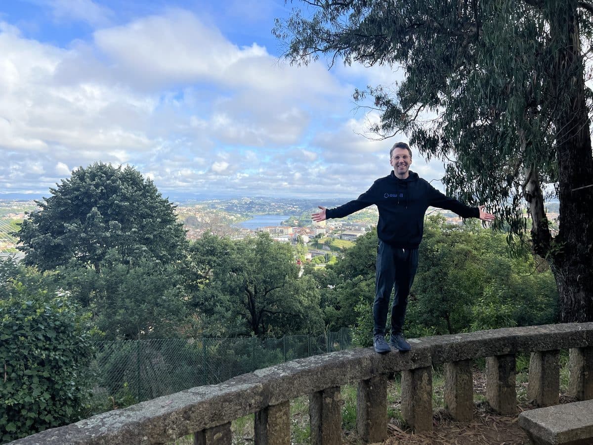 A person standing arms wide on a terrace above a wooded bay